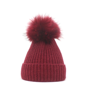 Close-up of wine red ribbed knit beanie featuring a large fluffy faux fur pompom on top