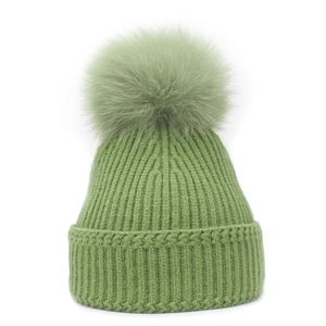 Close-up of light green knitted beanie with thick ribbing and large fluffy pompom top
