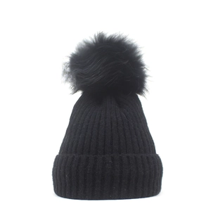Detailed close-up of a black ribbed knit beanie featuring a large faux fur pom-pom detail