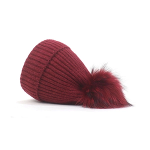 Detail of burgundy knitted winter beanie with a large faux fur pom-pom and ribbed texture