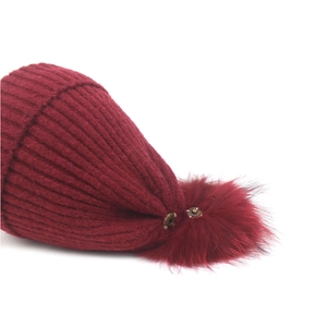 Close-up of the detachable faux fur pompom with metal snap button on a burgundy knit beanie
