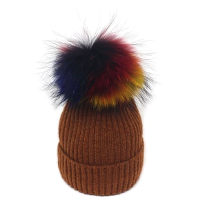 Détail de la texture en maille côtelée caramel et pompon en fausse fourrure coloré du bonnet