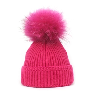 Close-up of ribbed knit texture and soft faux fur pom-pom on rose red winter beanie