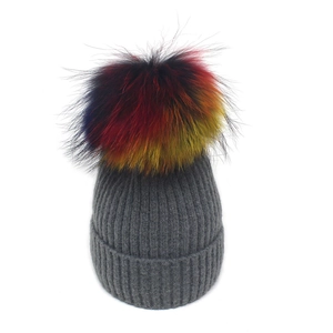 Détail du bonnet en maille grise orné d'un pompon en fausse fourrure multicolore éclatant