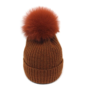 Close-up of caramel winter knit beanie featuring a large fluffy faux fox fur pom pom