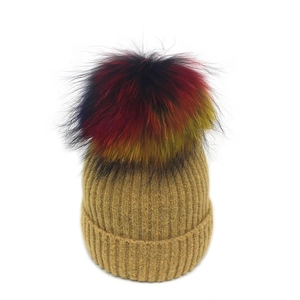 Détail du bonnet en maille côtelée kaki avec un grand pompon en fourrure multicolore