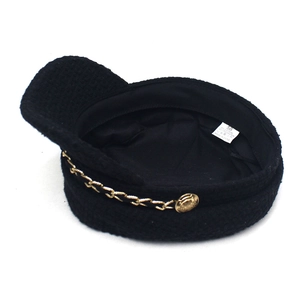 Dettaglio cappello newsboy in tweed nero con catena in metallo ed etichetta taglia 58