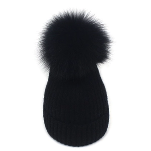 Detail of black cable knit beanie with fluffy faux fur pom-pom and folded cuff