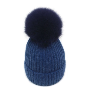 Detailed knit texture of dark blue winter beanie with large fluffy pom-pom on white background