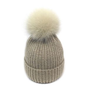 Detailed close-up of oatmeal winter knit beanie with vertical ribbed texture and fur pompom