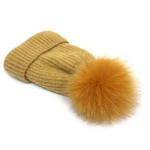 Detailed knit texture of mustard yellow winter beanie with large faux fur pom-pom
