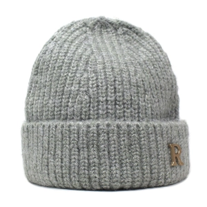 Close-up of dark grey knitted beanie with ribbed texture and golden R-letter metal badge