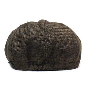 Detail of dark brown newsboy cap showing woven fabric texture and metal side emblem