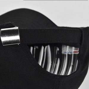 Detailed close-up of adjustable silver metal buckle and black twill fabric on baseball cap