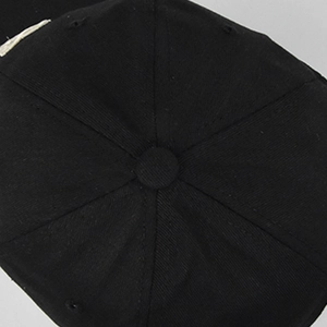Vista superior de gorra negra mostrando corona de seis paneles y botón central de tela