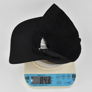 Detalle de una gorra de béisbol de algodón negro en báscula pesando 84,3 gramos