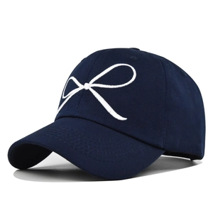 Détail de la broderie de nœud blanc sur une casquette en coton bleu foncé et coutures