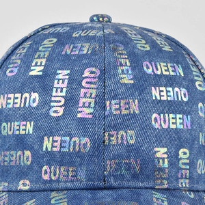 Macro detail of the iridescent QUEEN laser print on washed denim baseball cap texture