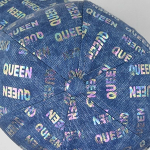 Macro detail of holographic QUEEN print on dark blue denim fabric of the baseball cap top