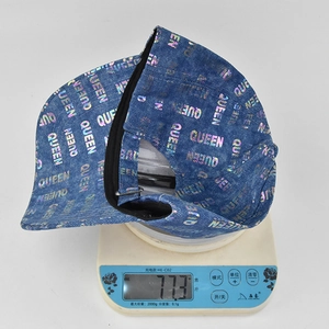 Detail shot of the QUEEN print denim baseball cap on a scale weighing 77.3 grams