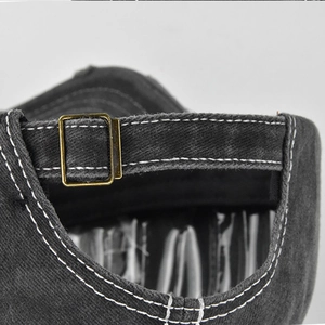 Detail of adjustable metal buckle and contrast stitching on washed denim baseball cap