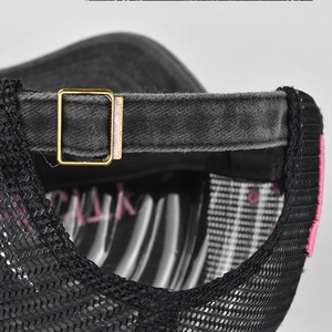 Detailed macro view of the black trucker hat with adjustable metal buckle and pink embroidery