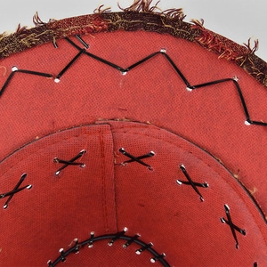 Macro detail of red cowboy hat featuring rustic black hand-stitched seams and fringe trim