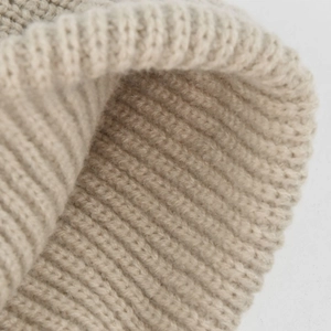 Dettaglio ravvicinato del berretto in maglia beige con trama spessa e bordo risvoltato