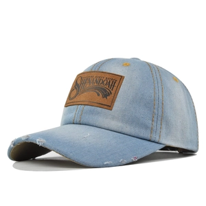 Detail showing distressed brim and vintage leather patch on light blue denim baseball cap