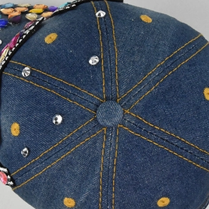 Detailed close-up of dark blue denim baseball cap with yellow stitching and rhinestones