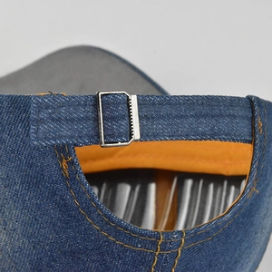 Detail showing blue denim fabric with orange lining and silver metal buckle on baseball cap