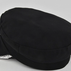 Detail of white lace trimming on a black flat-top sailor hat with bow accent