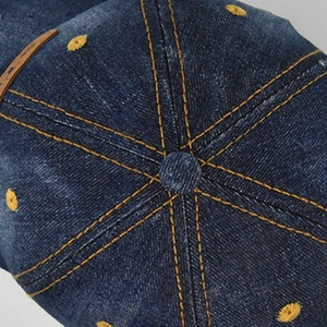 Close-up of vintage blue denim cap crown with orange contrast stitching and air eyelets