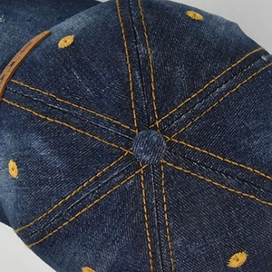 Top view detail of a distressed denim baseball cap with yellow stitching and embroidery