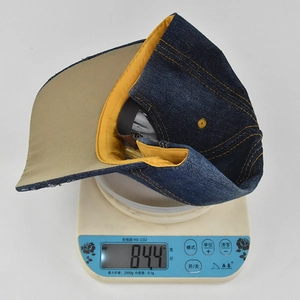Detail shot of distressed denim baseball cap showing contrast yellow stitching on scale