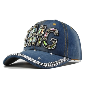 Dettaglio del cappello in denim blu con patch OMG in strass colorati e tesa borchiata