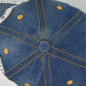 Dettaglio del cappellino in denim blu con cuciture gialle a contrasto e strass lucidi