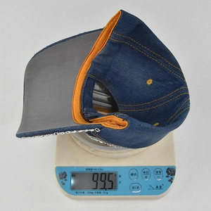 Visualizzazione del peso del berretto di jeans blu con bordo arancione e strass su scala