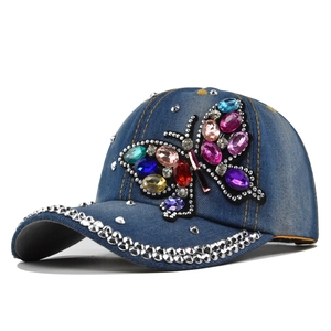 Detail of blue denim baseball cap featuring colorful rhinestone butterfly and metal rivets
