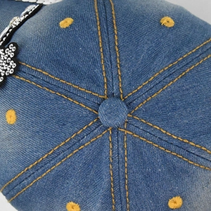 Detail of blue denim baseball cap showing contrast stitching and rhinestone crown pattern