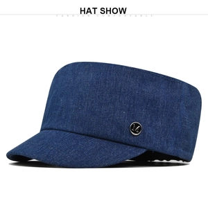 Detail van een blauwe denim flat-top pet met een zilveren metalen M-logo embleem