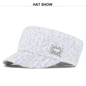 Detail of white floral cadet cap featuring blue patterns and a shiny rhinestone buckle