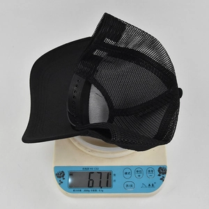 Digital scale showing the 67.1g weight of a black mesh snapback trucker baseball cap