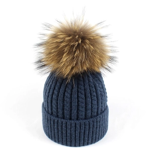 Dettaglio del berretto in maglia a trecce blu scuro con un morbido pompon in pelliccia marrone