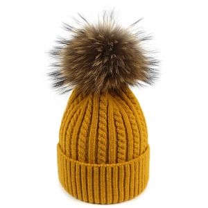 Dettaglio ravvicinato di un cappello di maglia giallo zenzero con pon pon di pelliccia
