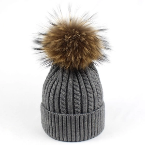 Dettaglio del berretto in maglia grigia con grande pompon soffice e bordo a coste