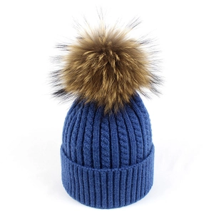 Dettaglio della maglia a trecce su berretto blu navy con un soffice pompon in pelliccia