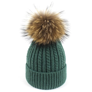 Dettaglio del cappello in lana di alpaca a trecce verde scuro con grande pompon di pelliccia