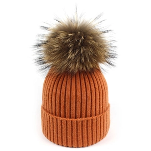 Detalle del gorro de punto acanalado naranja con un pompón de piel grande y borde doblado