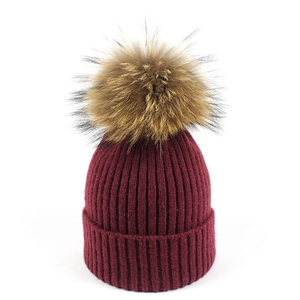 Detalle del gorro de punto granate con un pompón de piel de mapache suave y esponjoso
